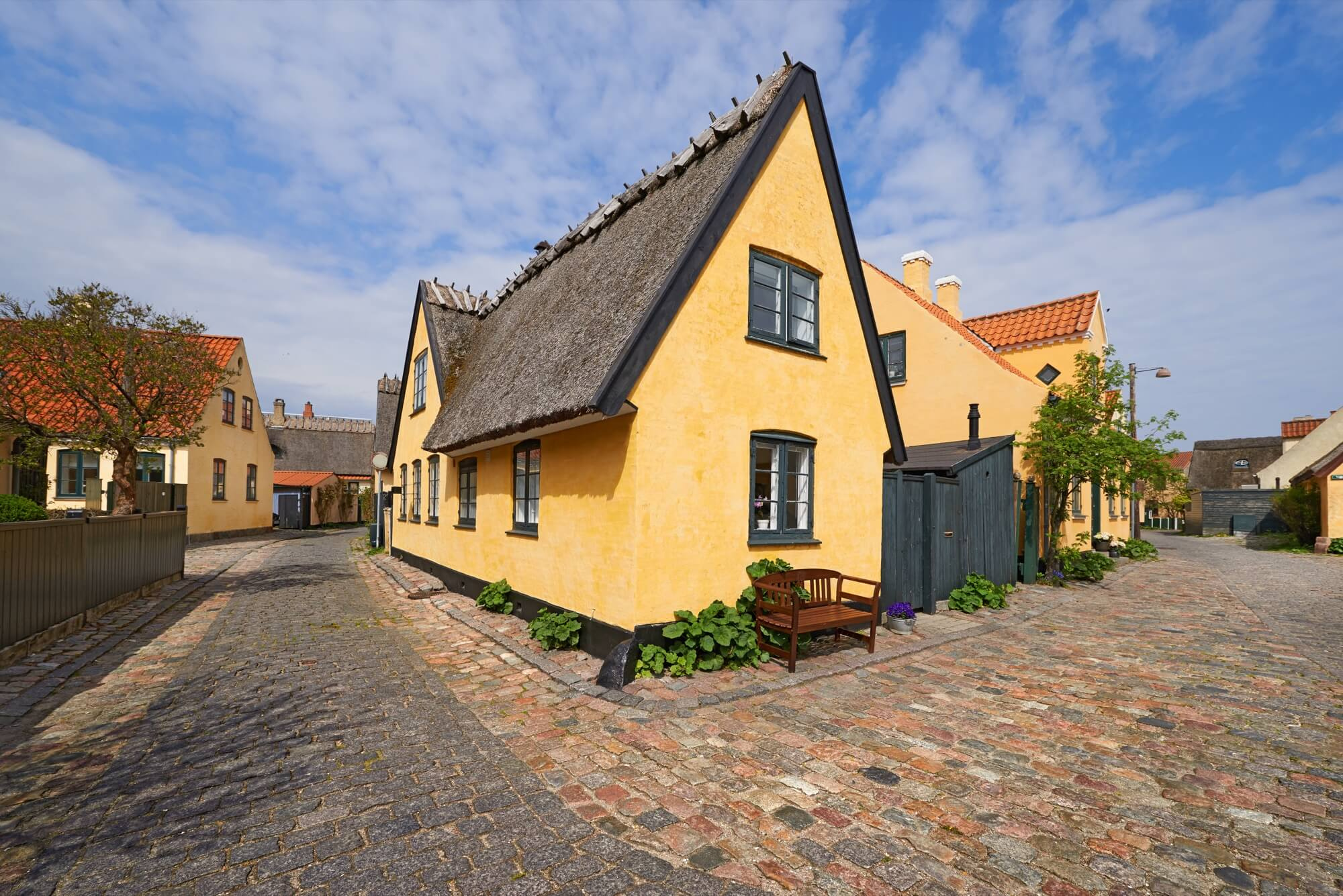 Traditionellt gult hus med halmtak och putsad fasad på en kullerstensgata efter renovering.