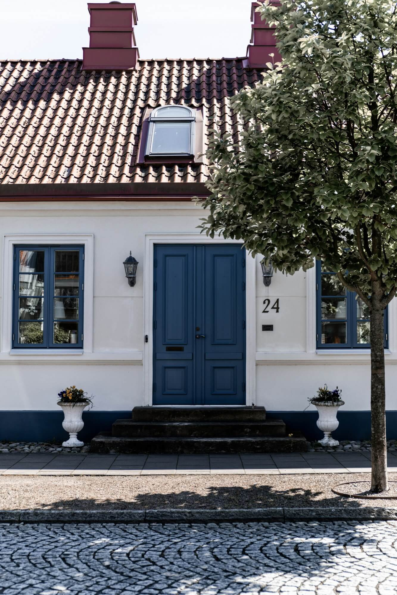 Vit fasad på hus med blå dörr och fönster, renoverad framsida med prydnadskruka.